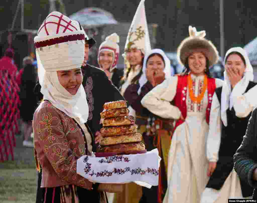 Young women in national dress wait to welcome guests with a stack of traditional bread.