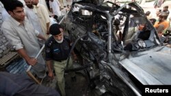 A policeman and residents gather near a damaged car at the site of the bomb blast near a religious school in Peshawar on May 24.