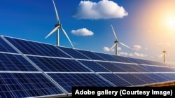 Сонячна ферма в сільській місцевості з величезними рядами панелей, що поглинають сонячне світло, оточена полями та вітровими турбінами на задньому плані