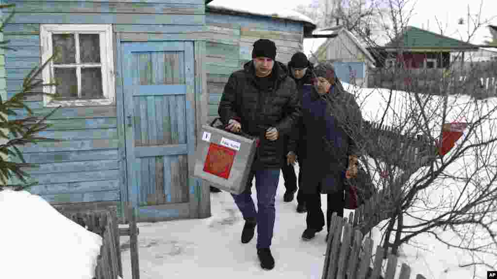 A választási bizottság tagjai házhoz mentek az idős szavazókhoz. A március 16-án készült képen a Moszkvától több mint kétezer kilométerre lévő szibériai Nyikolajevka faluban keresik fel a mozgásukban korlátozott oroszokat