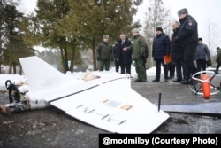 Чыноўнікам на беларускім палігоне паказалі зьбіты расейскі дрон «Гербера», а справа ад яго -- адзін з элемэнтаў дрона-перахопніка «Молат», 12 лютага 2026
