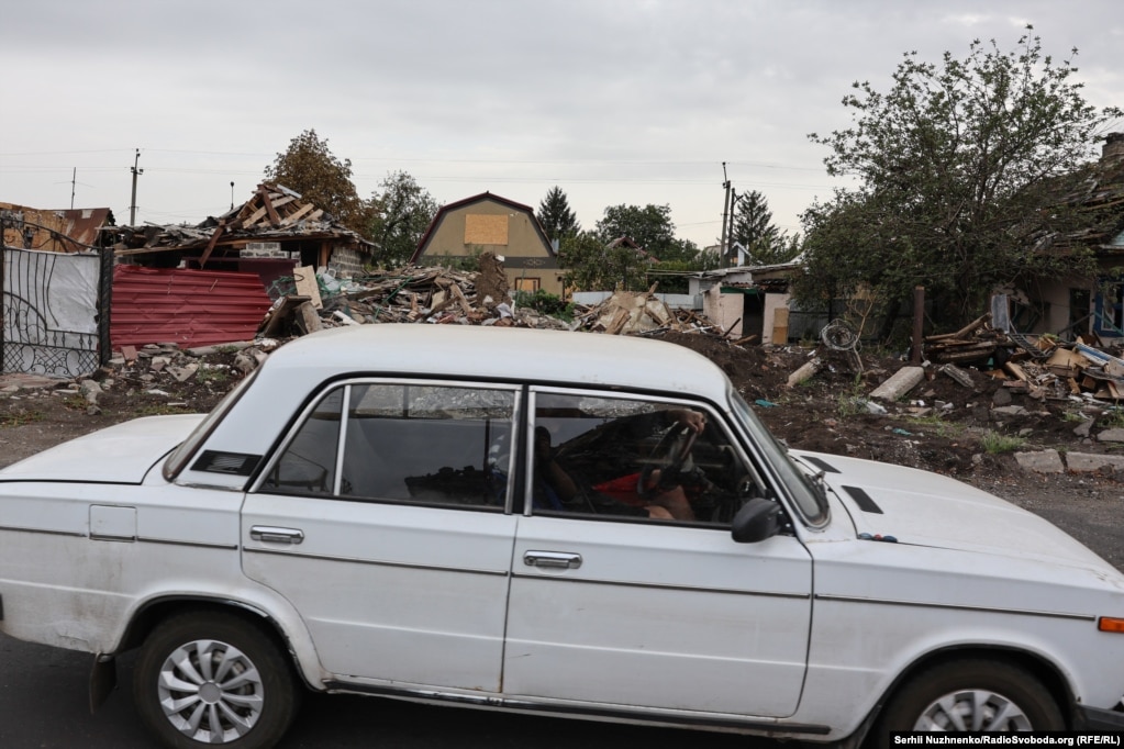 Një veturë duke kaluar pranë mbetjeve të ndërtesave të shkatërruara nga bombardimet.