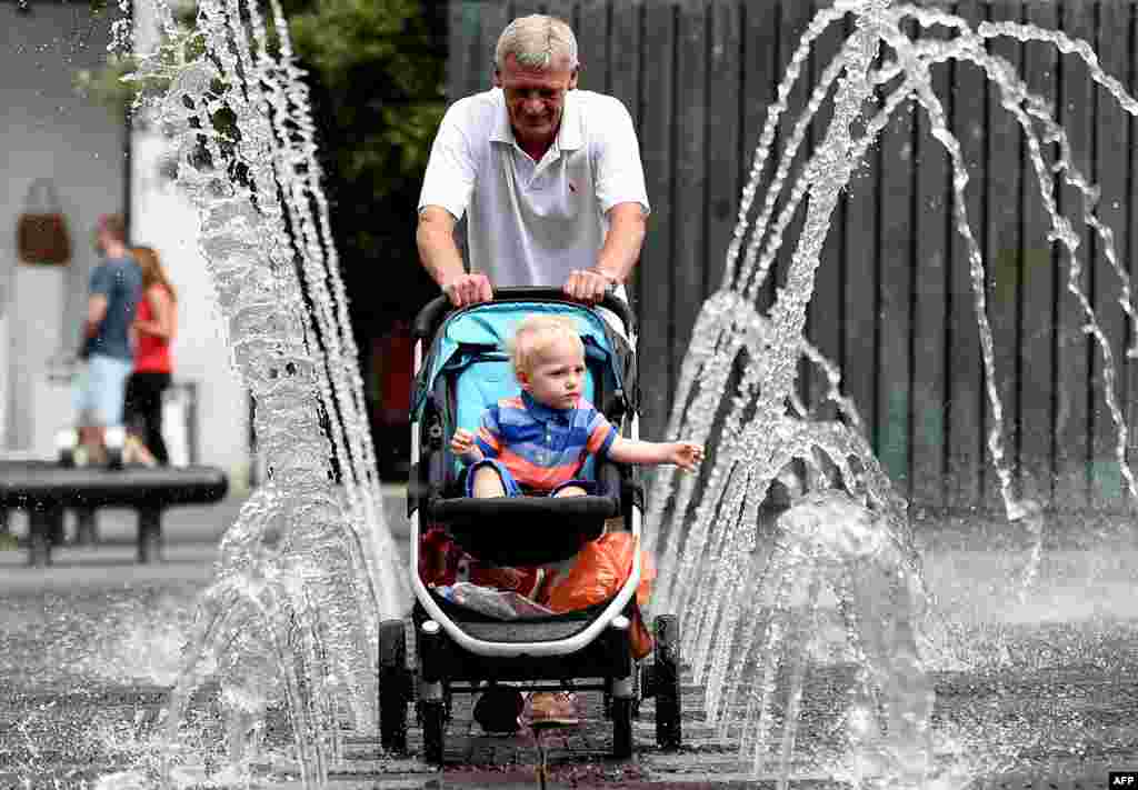 A man pushes a toddler in his pram through the middle of a pavement fountain in Liverpool, England. (AFP/Paul Ellis)