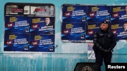 An EU policeman stands near a polling station in the northern part of the ethnically divided town of Mitrovica in November, with posters for Dimitrije Janicijevic behind him.