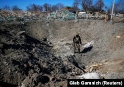 Un militar ucrainean inspectează un crater dintr-un sat din estul regiunii Kiev, 21 martie 2022.