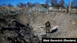 Украинский военнослужащий осматривает воронку от удара российских военных в селе на востоке Киевской области, 21 марта 2022 года