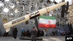 Iranians stand next to a mockup of a Kheibar missile in Tehran amid a fragile cease-fire in the Middle East. 