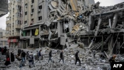 Disa palestinezë duke kaluar pranë ndërtesave të shkatërruara në Qytetin e Gazës më 3 mars 2024. 