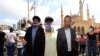 A man poses for a picture with a cardboard cut-out of Hassan Nasrallah (L), the head of Lebanon's Hezbollah, and former Foreign Minister Gibran Bassil hung by Lebanese protesters in downtown Beirut on August 8, 2020.