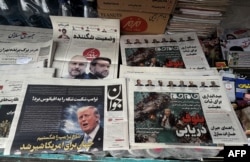 The front page of the Javan newspaper (left) and the front page of the Jam Jam newspaper, which features a cartoon of US President Donald Trump drowning in the Strait of Hormuz with the headline “Marine Bluff,” are pictured at a newsstand in Tehran on April 13.