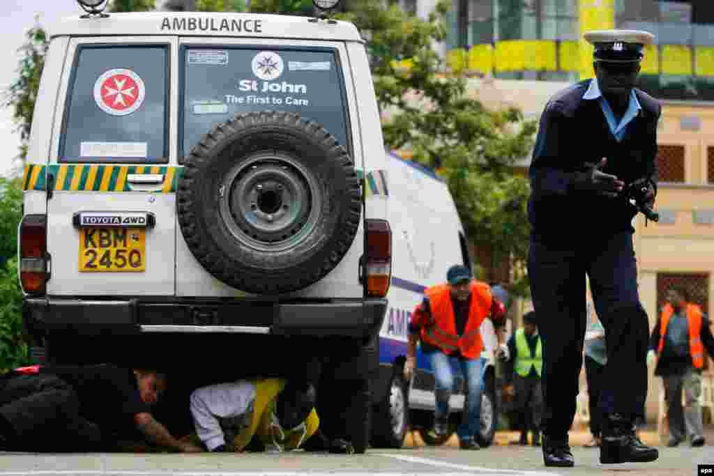 A Kenyan officer and others run for cover at the Oshwal Center adjacent to the Westgate shopping mall as the hostage crisis continues on September 23.