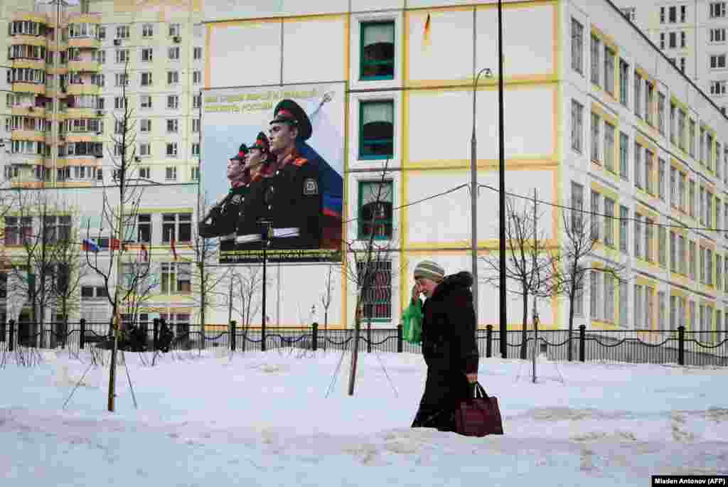 A woman carrying bags of food walks past a school building decorated with a military themed poster on the outskirts of Moscow, Russia. (AFP/Mladen Antonov)