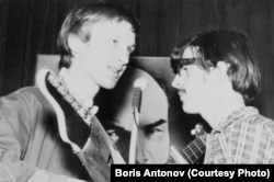 A young Boris Antonov plays guitar with a bandmate and a poster of Lenin in the background.