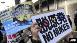 Protesters hold placards while marching in front of Tokyo Electric Power Company headquarters during a rally in the Japanese capital today.