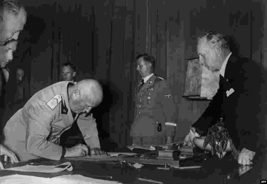 Italian Prime Minister Benito Mussolini signs the Munich Agreement as Martin Bormann (second right) and Joachim von Ribbentrop (right) look on.