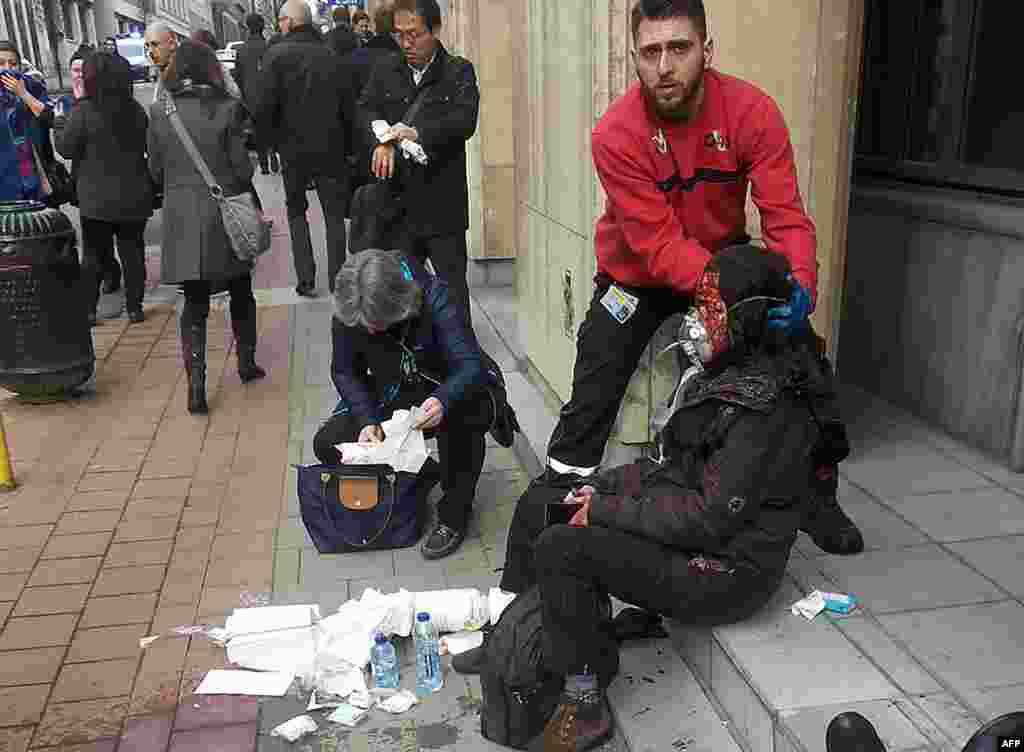 Hususy howpsuzlyk goragçysy Maalbeek metro stansiýasynyň daşynda ýaralanan aýala kömek edýär. (AFP/Michael Villa)