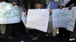 A young child holds a placard while posing with tribesmen as they stand on a NATO flag during a demonstration in Islamabad following the deadly air strike.