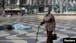 Жінка в масці проходить поруч із безпритульним у столиці Португалії Лісабоні, березень 2020 року