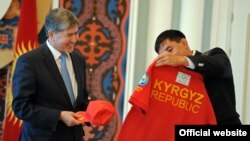 Капитан национальной олимпийской команды КР борец Данияр Кобонов вручил президенту КР Алмазбеку Атамбаеву памятную кепку и футболку с олимпийской символикой, Бишкек, 16 июля
