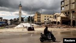 Un bărbat trece cu motocicleta pe lângă dărâmăturile unui șantier avariat în urma unui atac israelian în Nabatieh, Liban, pe 25 martie.