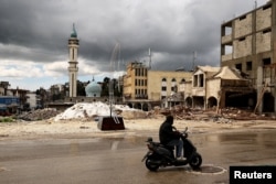 Čovek vozi motocikl pored ruševina posle izraelskog napada u Nabatiji, u Libanu, 25. marta.