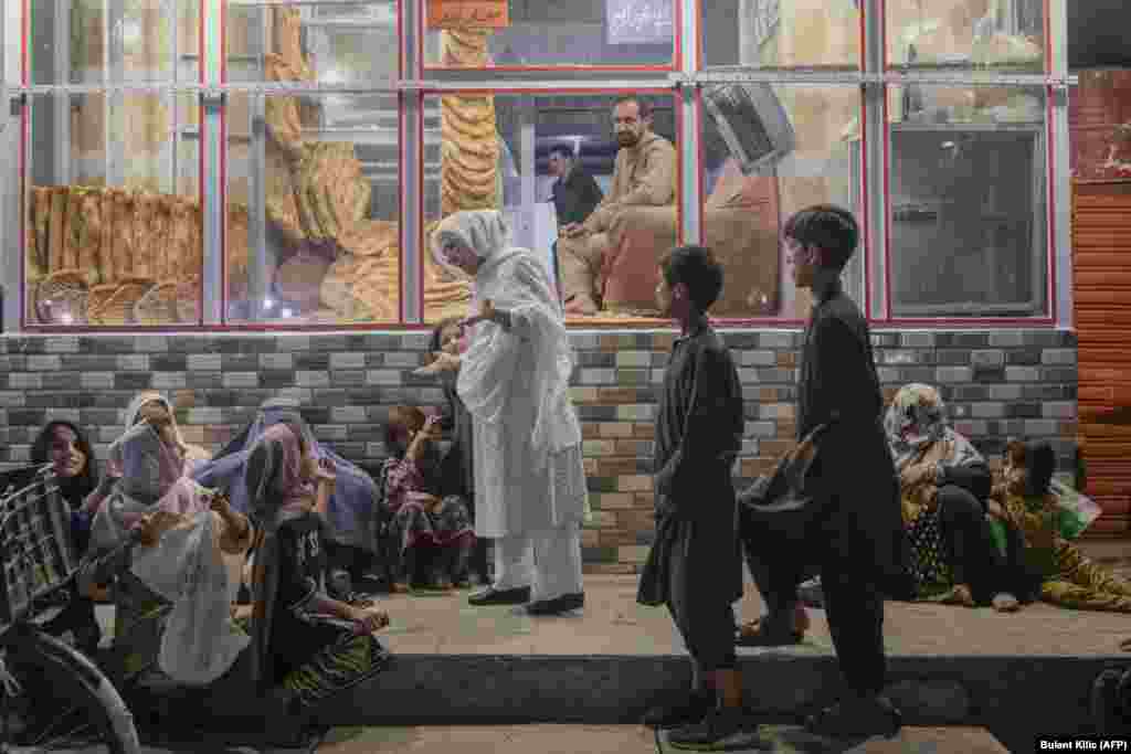 An Afghan woman talks to young people in need after giving them bread in front of bakery in Kabul.