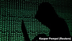 ILLUSTRATION -- FILE PHOTO: A hooded man holds a laptop computer as cyber code is projected on him in this illustration picture taken on May 13, 2017. 