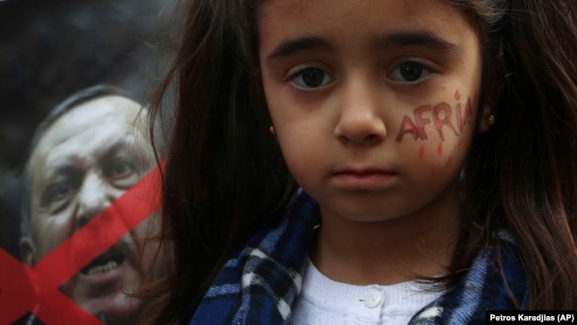 Një vajzë kurde që jeton në Qipro ka të shkruar në fytyrë “Afrin” dhe qëndron pranë një posteri të presidentit turk, Recep Tayyip Erdogan, gjatë një proteste kundër operacionit turk në Afrin të Sirisë.