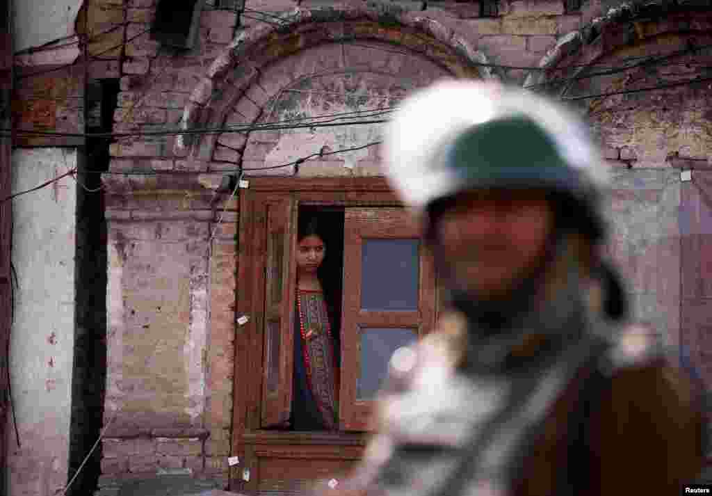 An Indian police officer stands guard as a girl peeps from the window of her house after Kashmiri separatists called for a day-long strike in protest at recent killings in the restive region, which is claimed by both New Delhi and Islamabad. (Reuters/Danish Ismail)