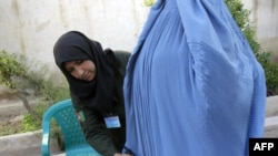 An Afghan policewoman searches a burqa-clad woman entering a polling station in Herat in August 2009 voting.