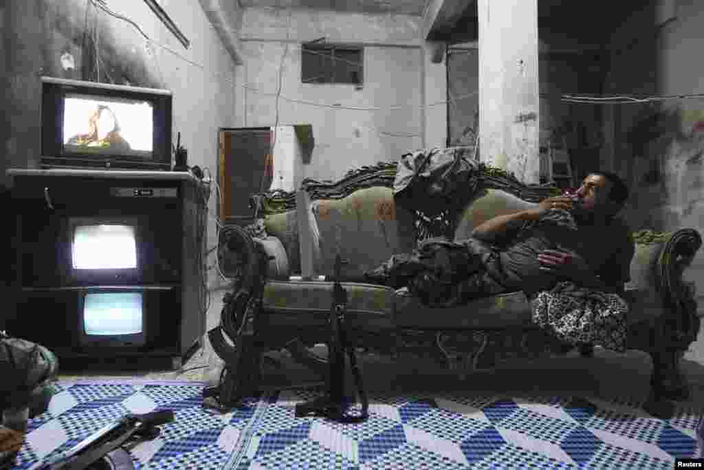 A Free Syrian Army fighter rests on a sofa as he watches television and surveillance monitors inside a room in Aleppo's Karm al-Jabal district. (Reuters/Muzaffar Salman)