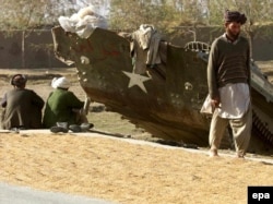 Мужчины-афганцы сушат рис у разбитого бронетранспортера , 15 ноября 2001 года. Иллюстративное фото.