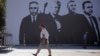 A pedestrian in Pristina walks past a banner depicting four Kosovo war crimes suspects, including former Kosovo President Hashim Thaci, who are standing trial in The Hague. 
