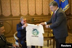 Pre;edintele Petro Poroșenko oferindu-i un T-shirt cu un portret al lui Oleg Sențov cântărețului pop Elton John într-o întâlnire la Kiev, 12 sept., 2015.