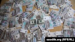 Банкноты номиналом тысяча узбекских сом вокруг банкноты в сто долларов США.
