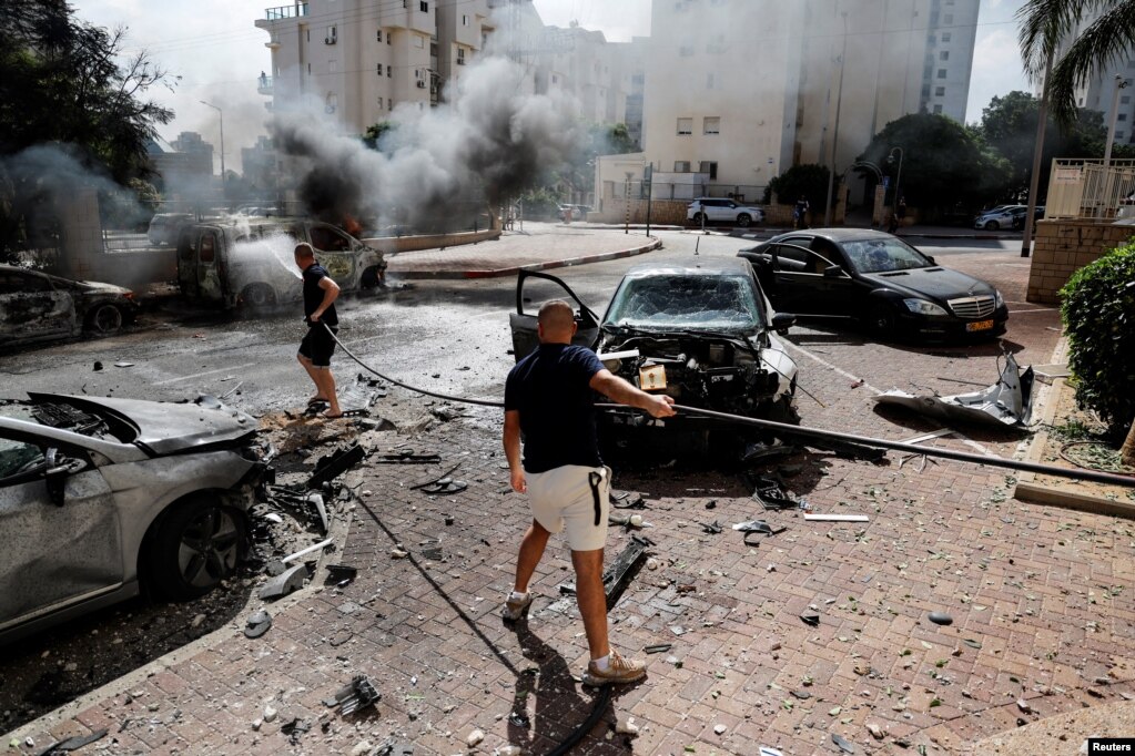 Qytetarët shuajnë makinat e djegura, që u goditën nga raketat e lëshuara nga Gaza. Ashkelon, 7 tetor 2023. 