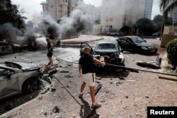 Жители Ашкелона тушат горящий после ракетного обстрела автомобиль. 7 октября 2023 года. Фото: Reuters