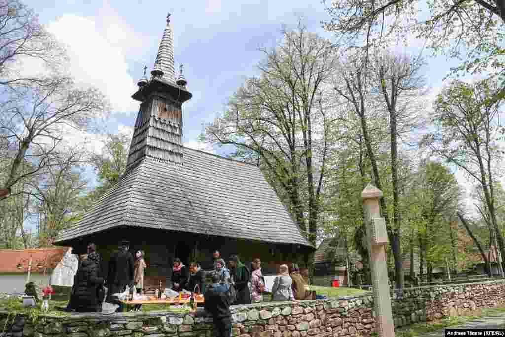 Un grup de oameni discută după o slujbă religioasă lângă o biserică din lemn, în Muzeul Satului din București.