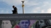 A man stands next to a billboard in Kyiv showing the British , U.S., and Ukrainian banknotes.