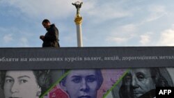 A man stands next to a billboard in Kyiv showing the British , U.S., and Ukrainian banknotes.