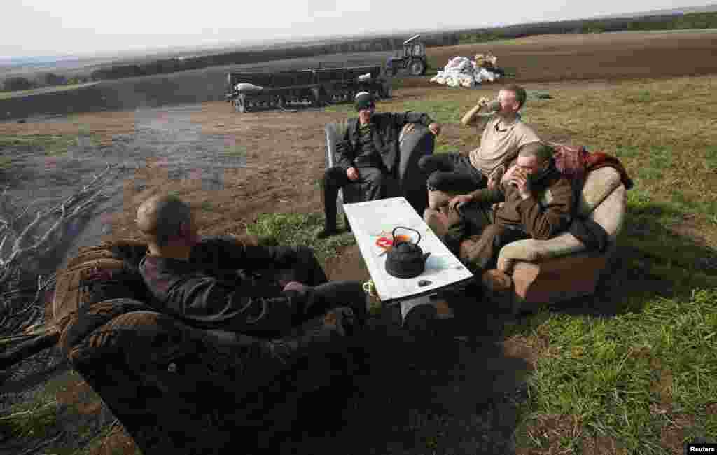 Inmates sit on a sofa and armchairs in a field while having a meal during a work break.