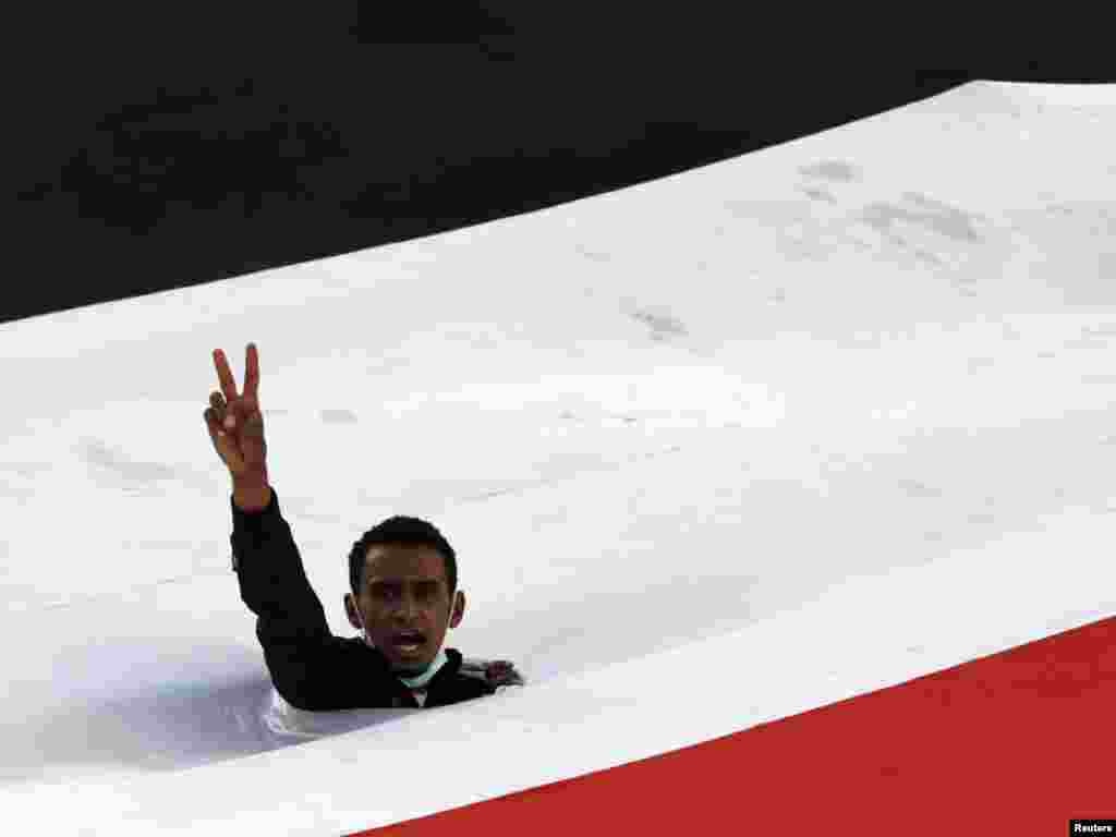 An antigovernment protester flashes the victory sign as he emerges through a gap in Yemen's national flag during a demonstration in Sanaa on April 4. Police and armed men in civilian clothes opened fire on antigovernment demonstrators in the Yemeni cities of Taiz and Hudaida, witnesses said, as a drive to oust the president gathered pace. Photo by Khaled Abdullah for Reuters