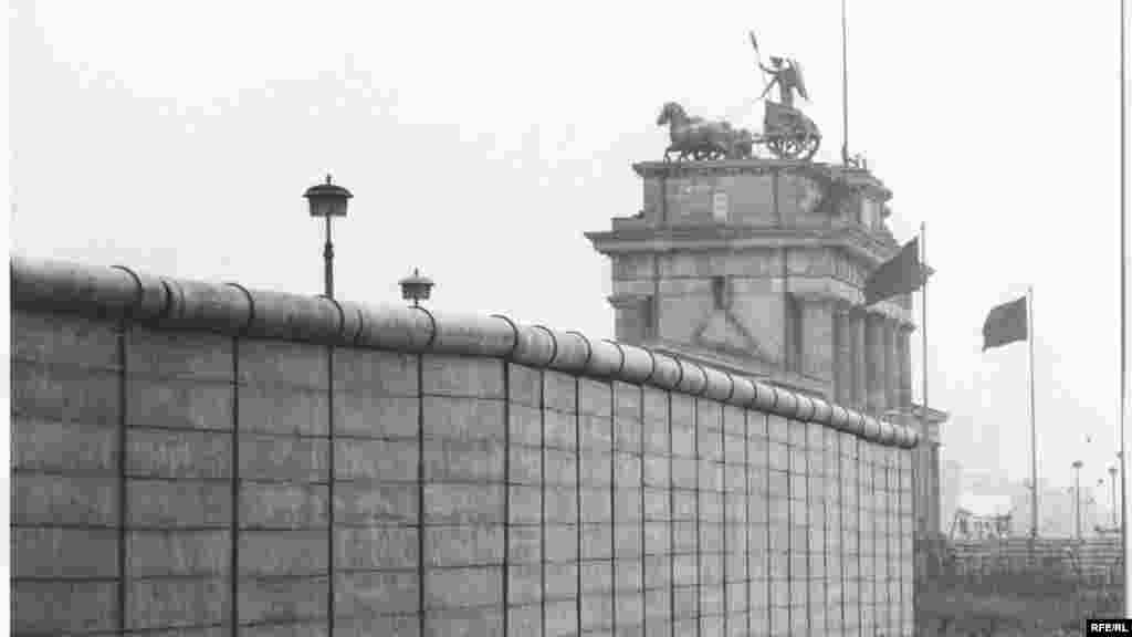 A fal a Brandenburgi kapuval a háttérben.&nbsp;A berlini fal 155 kilométer hosszan húzódott át a városon, 13 ellenőrző ponttal és 302 őrtoronnyal.
