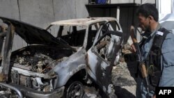 An Afghan policeman stands guard near the wreckage of a burned-out vehicle at UN headquarters in Mazar-e Sharif on April 2.