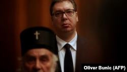 Președintele Serbiei, Aleksandar Vucic (în fundal) ascultându-l pe Patriarhul Irinej vorbind