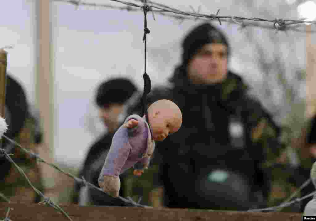 A doll placed by stranded Iranian migrant protesters hangs from barbed wire in front of Madedonian police at the Greek-Macedonian border near to the Greek village of Idomeni. (Reuters/Yannis Behrakis)