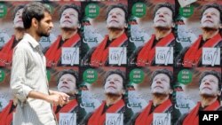 A Pakistani man walks past electoral posters of Pakistani politician and former cricketer Imran Khan, in Karachi.