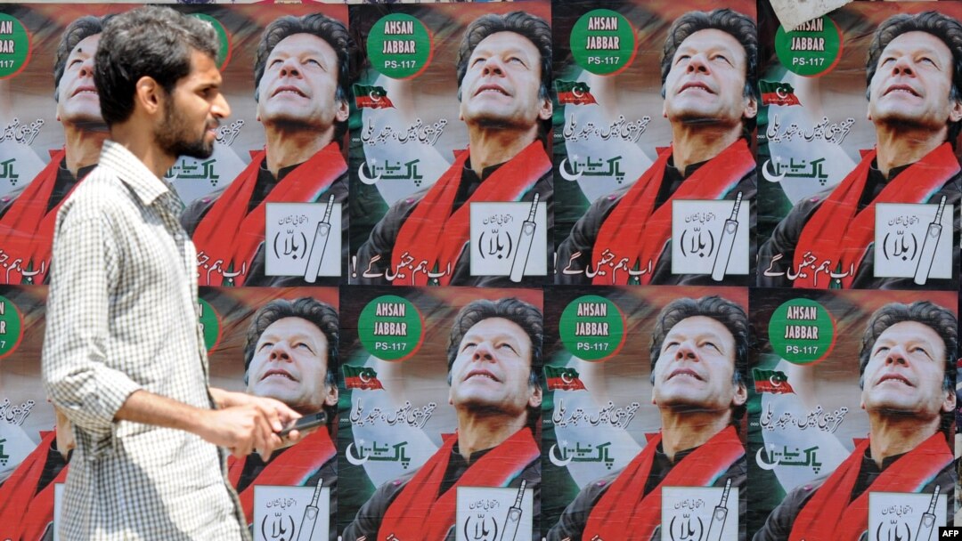 A Pakistani man walks past electoral posters of Pakistani politician and former cricketer Imran Khan, in Karachi.