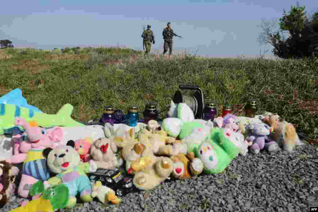 Pro-Russian armed rebels walk near stuffed animals and candles left at the site of the MH17 flight crash in Ukraine&#39;s Donetsk region. (AFP/Aleksey Filippov)