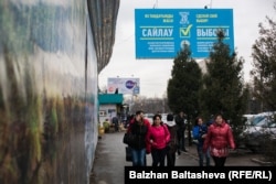 Люди проходят мимо агитационного билборда, призывающего пойти на досрочные выборы мажилиса парламента и очередные выборы маслихатов в Казахстане. Алматы, 18 марта, 2016 года